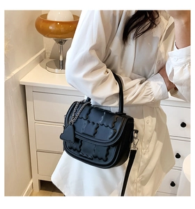 Detail of black leather handbag with embossed texture, heart charm and shoulder strap