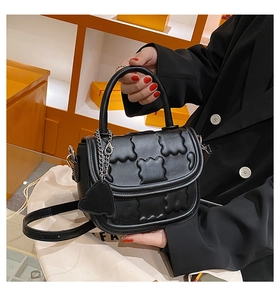 Detailed macro view of the embossed cloud texture and bear charm on a black leather handbag