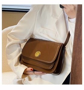 Brown quilted crossbody bag with golden buckle on a model in white blazer