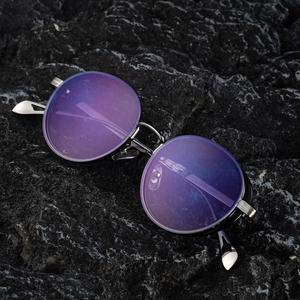 Steampunk round metal sunglasses with purple lenses on a volcanic rock background