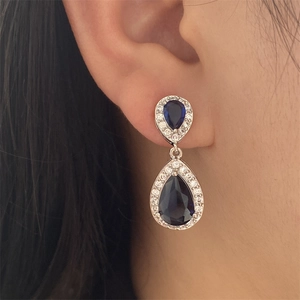 Macro detail of tear-drop dark blue sapphire earrings with white zircon halo on a model