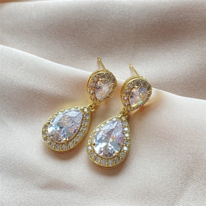 Detail of halo drop earrings with white cubic zirconia on gold metal over champagne silk