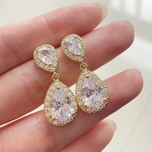 Sparkling double teardrop zircon earrings with golden base shown held in hand