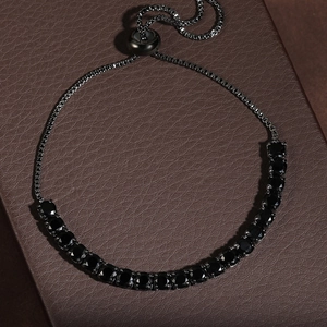 Dettaglio del bracciale regolabile con cristalli neri e catena box su scatola in pelle