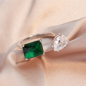 Macro detail of geometric open ring with emerald-cut green stone and pear-shaped zircon