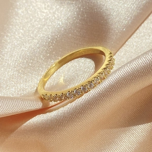 Elegant gold finish ring with minimalist round zircon row on silky satin background