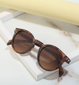 Detail of tortoiseshell round frame sunglasses with brown gradient lenses and gold hinge