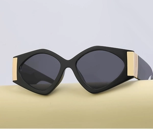 Close-up of cat-eye sunglasses with bold gold metal hinge detail and sleek black frame