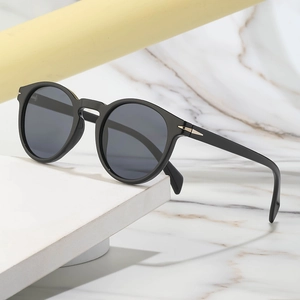 Retro black round frame sunglasses with signature gold metal arrow accent on marble stand