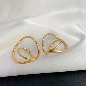 Detail of gold Mobius ear clips with double-layered geometric wire design on white silk