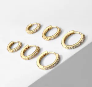 Three pairs of gold-plated cubic zirconia hoop earrings on a white marble display stand