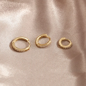 Detailed view of three sizes of gold huggie earrings with micro-pave white zircons