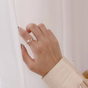 Detail of double pearl gold open ring with crystals worn on a finger in soft lighting