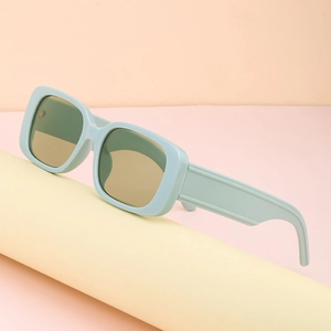 Trendy small square mint green sunglasses with wide legs on a beige cylinder stand