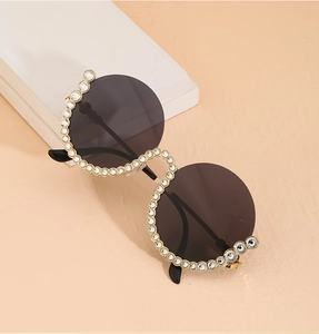 Detailansicht der modischen runden Sonnenbrille mit Goldrahmen, Strasssteinen und Kette