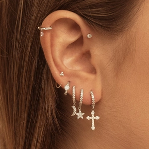 Macro view of geometric silver earrings set with moon, star, and cross zircon pendants