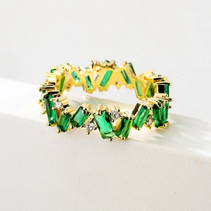 Macro shot of gold eternity ring with emerald green rectangular gems and white diamonds