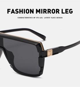 Detail of glossy black sunglasses with gold metal trim and embossed rivet on temple