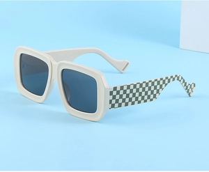 Détail de lunettes de soleil oversize crème avec motif damier vert et blanc sur les branches