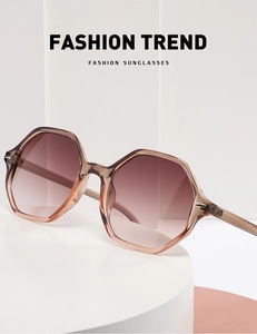 Close-up of retro hexagonal sunglasses with brown gradient lenses on a white pedestal