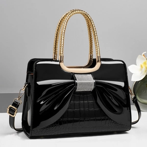 Detailed view of black patent leather bag with rhinestone bow and gold chain handle