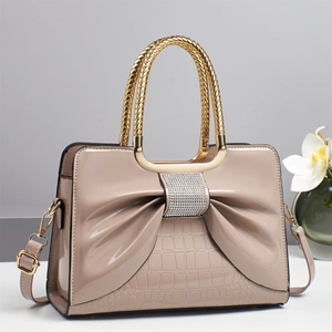 Detail showing nude patent leather handbag with rhinestone bow and croc texture