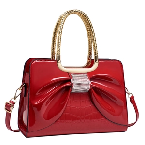 Red patent leather handbag with oversized bow and rhinestone trim on white background