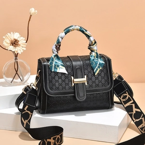 Detail of black patterned handbag featuring golden H-clasp and elegant silk scarf handle