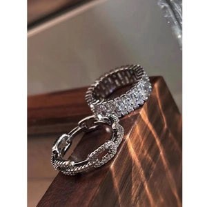 Close-up of sparkling silver hollow chain ring and zircon band on dark wood surface