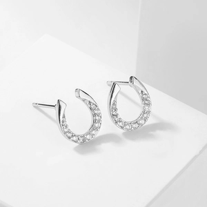 Close-up of silver horseshoe stud earrings with sparkling cubic zirconia on a white pedestal