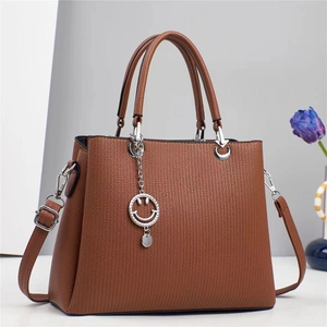 Detail of caramel faux leather shoulder bag featuring crosshatch texture and silver charm