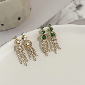 Detailed view of long gold tassel earrings with clear and emerald green crystals