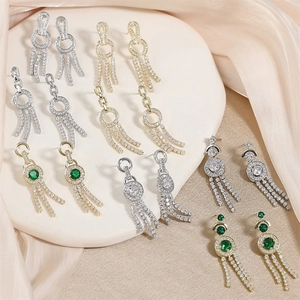 Elegant long tassel earrings with green gemstones and white crystals on silk background