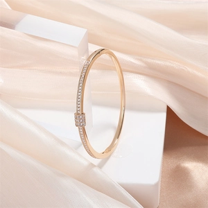 Bracelet doré serti de zircons avec breloque cylindrique sur support blanc