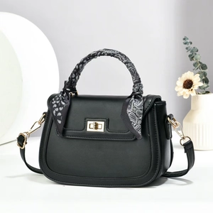 Elegant black saddle bag with silk scarf handle and gold buckle in a minimalist setting