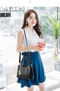 Close-up of black handbag with wavy embossed pattern and golden leaf pendant on a model