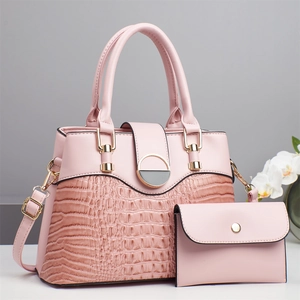Rosa Handtasche mit Krokodilprägung im Set mit Geldbörse und goldenen Details vor grau
