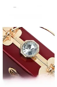 Detail of red patent leather evening bag featuring a large glass diamond and gold hardware