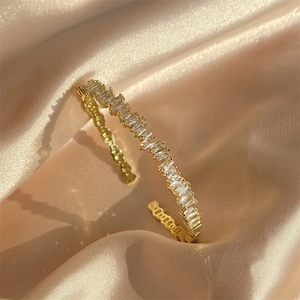 Elegant gold open bangle with geometric baguette zircons on premium silk background