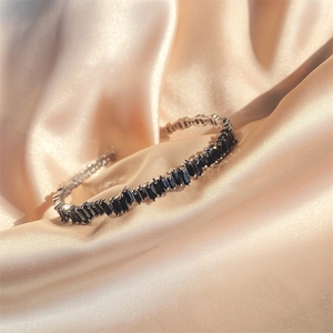 Close-up of silver bangle with rectangular black zircons on champagne silk fabric