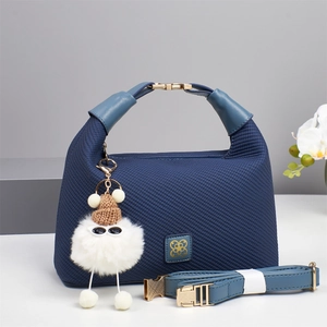 Detail of navy blue quilted shoulder bag with gold logo and white plush monster charm