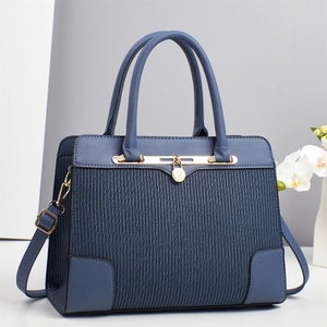 Detail of blue paneled tote bag featuring pleated texture and gold logo pendant