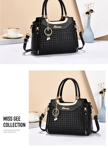Detail of black tote bag with woven texture panel and golden clover charm on metal handle