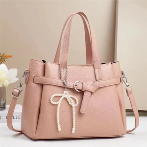 Detail of pink crossbody bag with litchi grain texture and pearl bow pendant accent