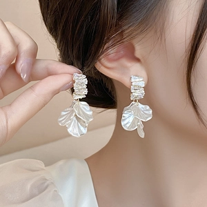 Macro detail of silver tassel earrings with shell petals and square-cut diamonds on model