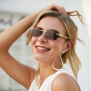 Detail of gold C-hinge on frameless wood grain sunglasses worn by a blonde model
