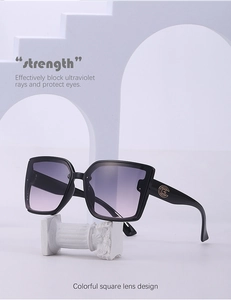 Détail de lunettes de soleil carrées noires avec verres dégradés violets et logo en métal