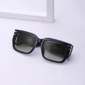 Detail of black oversized square sunglasses with gold T-shaped metal hinge accents