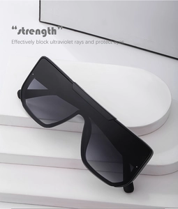 Flat top oversized sunglasses on a minimalist white geometric stand with modern grey lenses