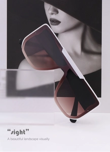Artistic detail of white oversized sunglasses with brown gradient lenses on acrylic